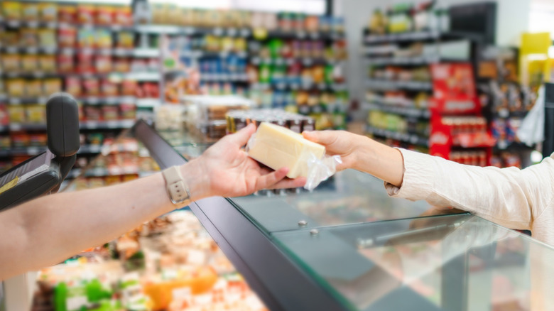 A deli counter worker hands a customer a packaged chunk of cheese over the counter