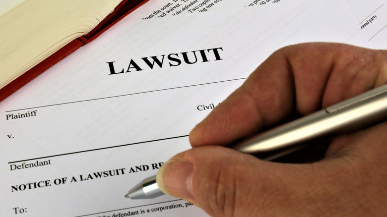 Someone holding a pen filling out lawsuit paperwork