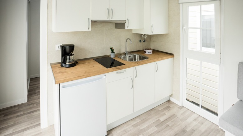 A very small off-white and beige kitchen with a wooden countertop