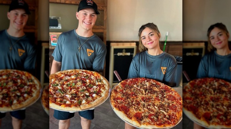 Graffiti Pizza employees holding two huge pizzas