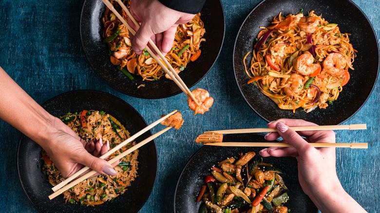 Hands holding chopsticks over bowls of Chinese takeout