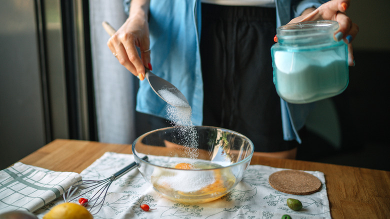Woman adding sugar to bowl while baking