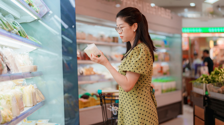 A woman is selecting tofu in the refrigerated section
