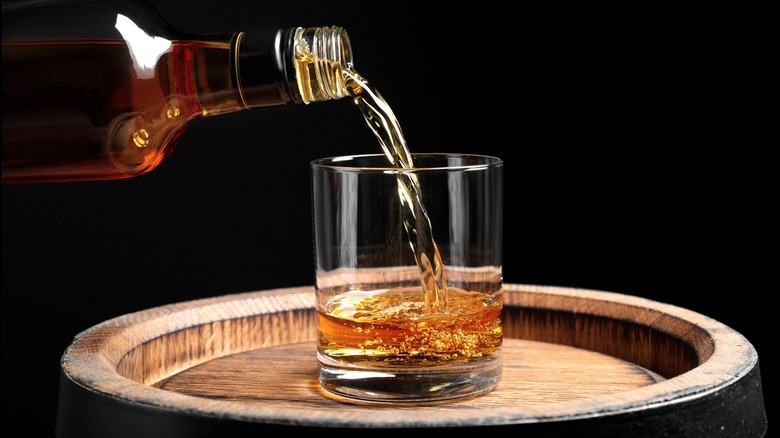 Whiskey being poured into a glass on a barrel