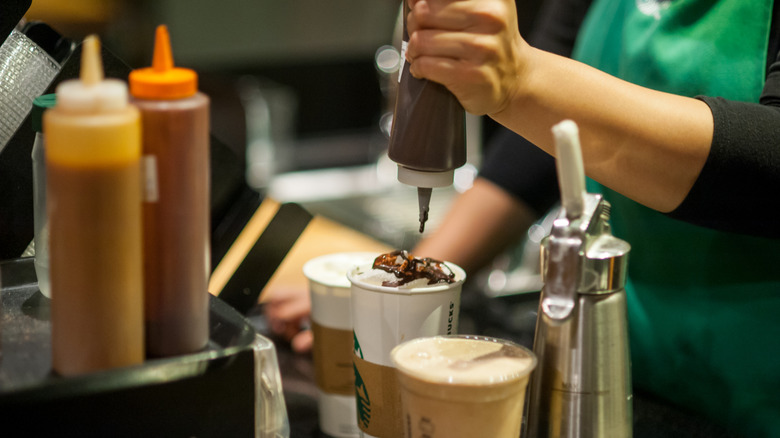 Starbucks employee putting mocha sauce on drink