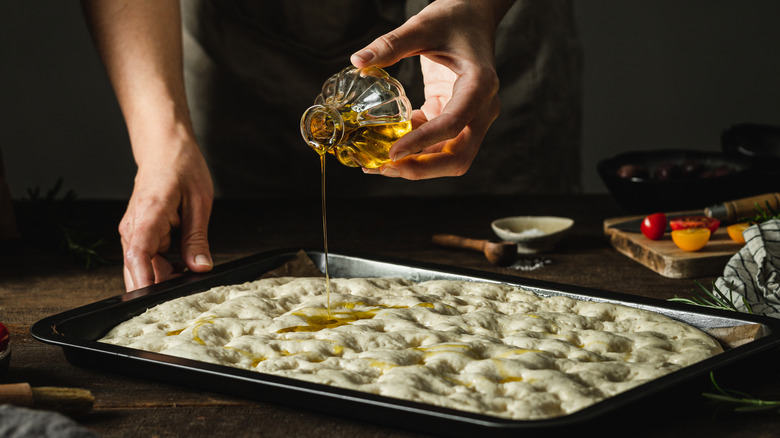 Baker adding oil to focaccia dimples 
