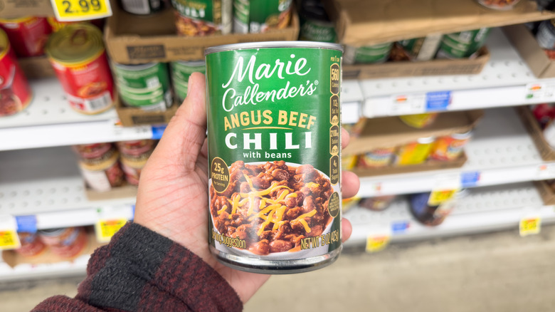 Hand holding a can of Marie Callender's Angus Beef Chili in a grocery store