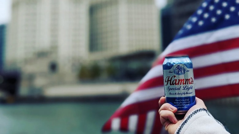 Can of Hamm's Special Light held up in front of a flag