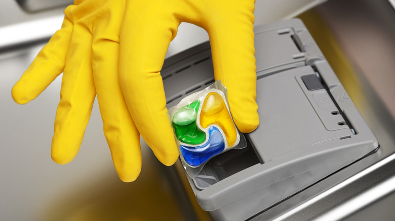 Closeup up person with gloved hand placing dishwasher pod in dishwasher