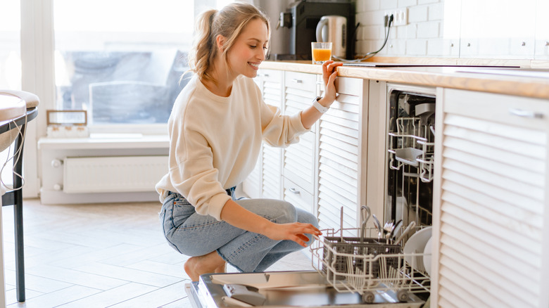 Woman crouching to open dishwasher