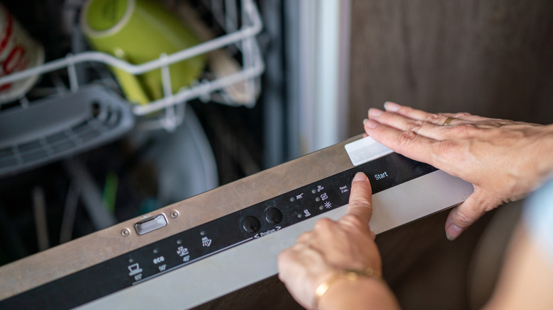 A close-up of a woman's hand selecting a dishwasher setting