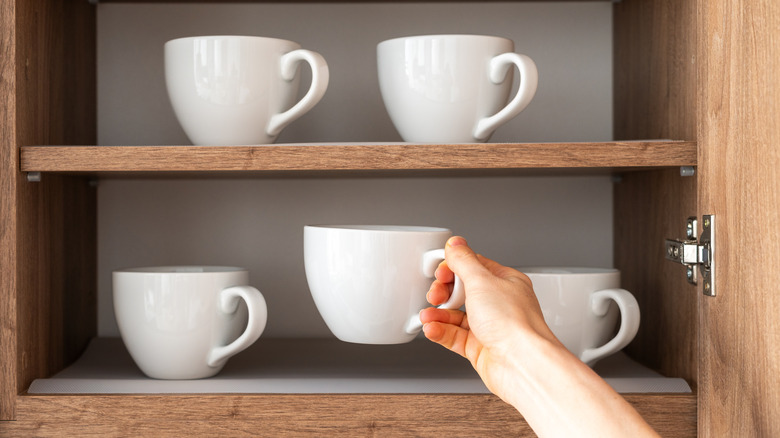 Hand taking mug from cabinet shelf