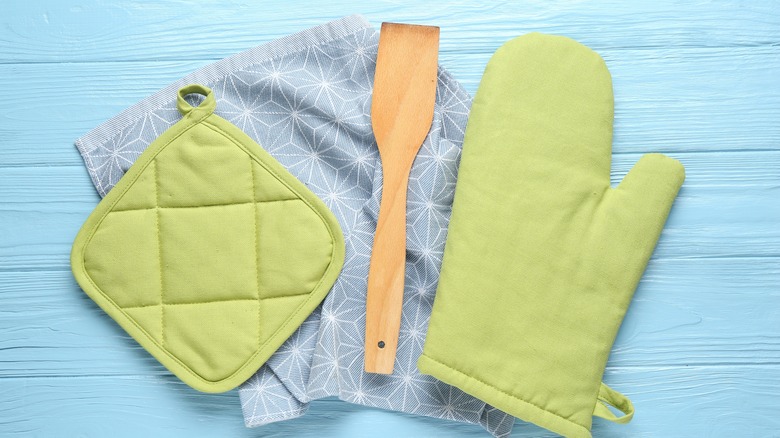 Green oven mitt and pot holder next to wooden spatula sitting on light blue towel