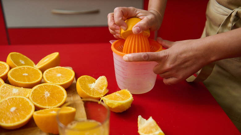 a person hand-juicing fresh oranges on a red countertop