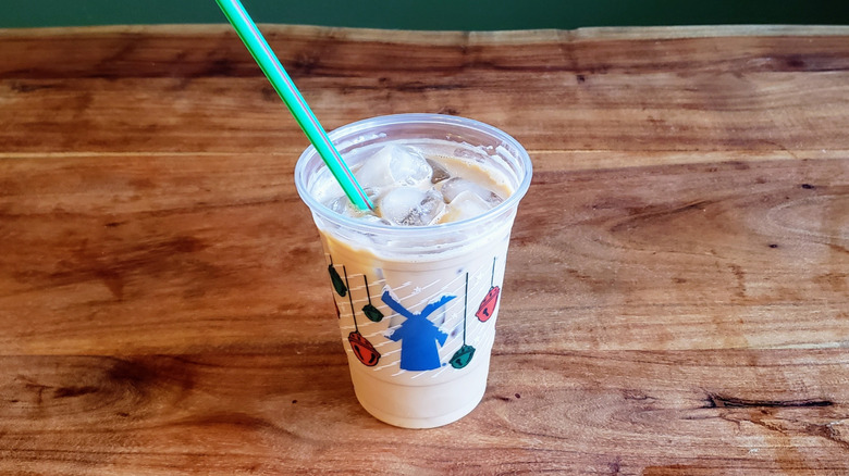 A Dutch Bros Iced Vanilla Protein Coffee on a wooden table with a straw but no lid