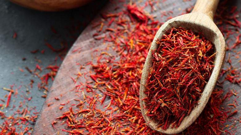 Dried saffron spice in wooden spoon and scattered on table