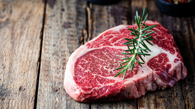 A raw ribeye with a sprig of rosemary on it