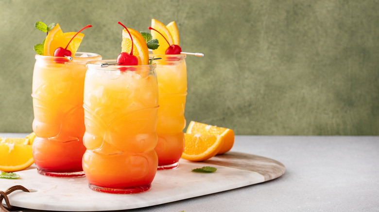 Three pretty orange tiki cocktails on a tray.