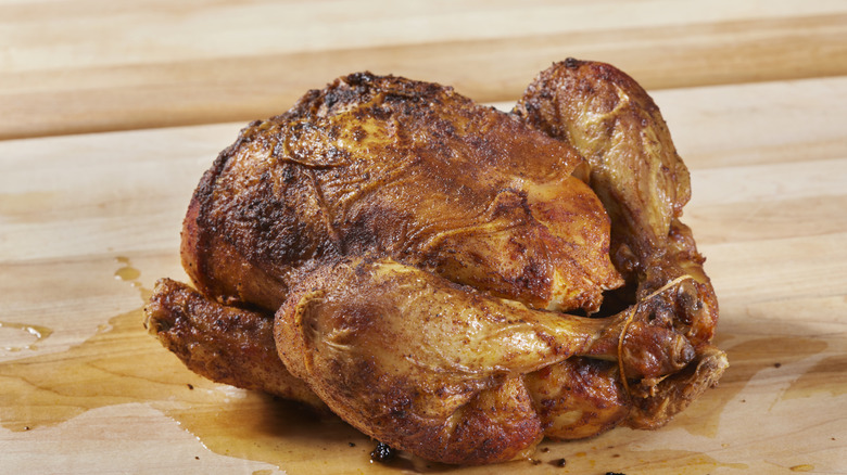 A rotisserie chicken with golden skin sitting on a cutting board