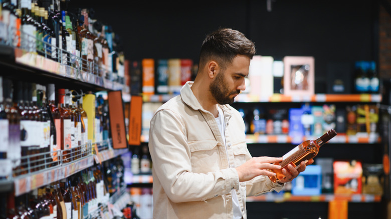 man inspects a bottle of liquor in a supermarket