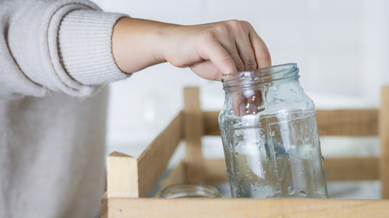 A person placing a large wet jar in a wooden rack