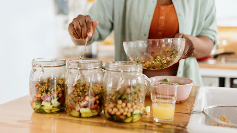 A woman spooning food into three large clear glass jars
