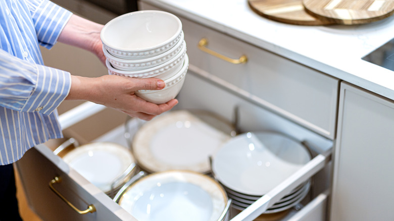 View of person holding stack of bowls over a kitchen cabinet drawer
