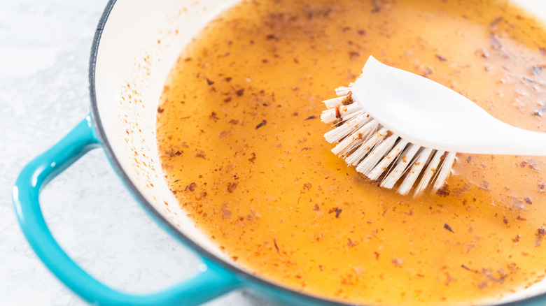 Overhead view of cleaning an enameled cast iron pan with a scrub brush