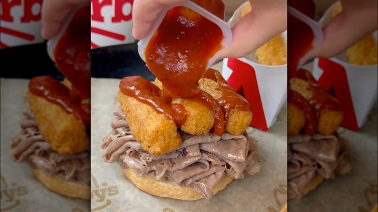 Drizzling marinara over roast beef sandwich