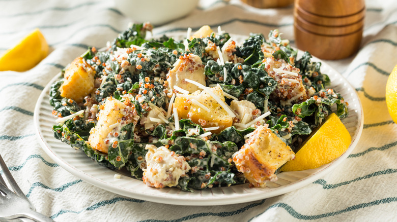 Kale and quinoa Caesar salad on plate with lemon wedges