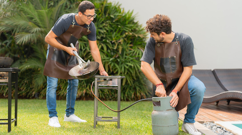 two men in a backyard getting a propane tank set up to a grill