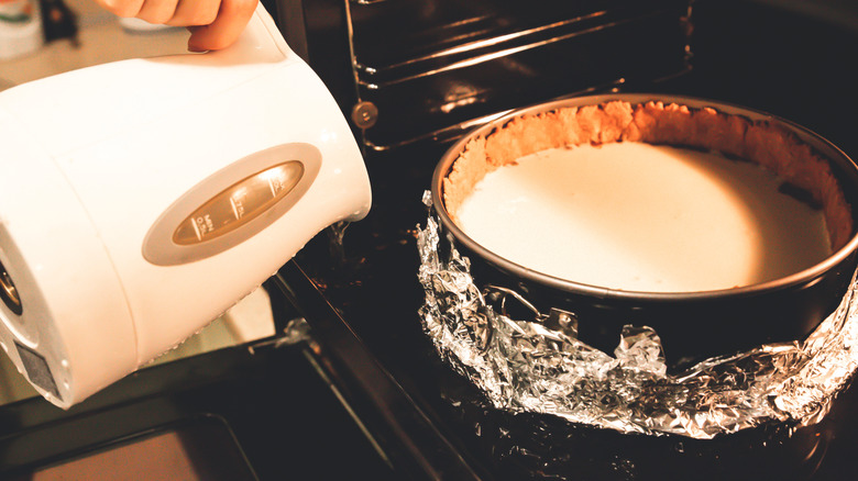 Someone pours water from a kettle into a bain-marie holding a cheesecake in the oven