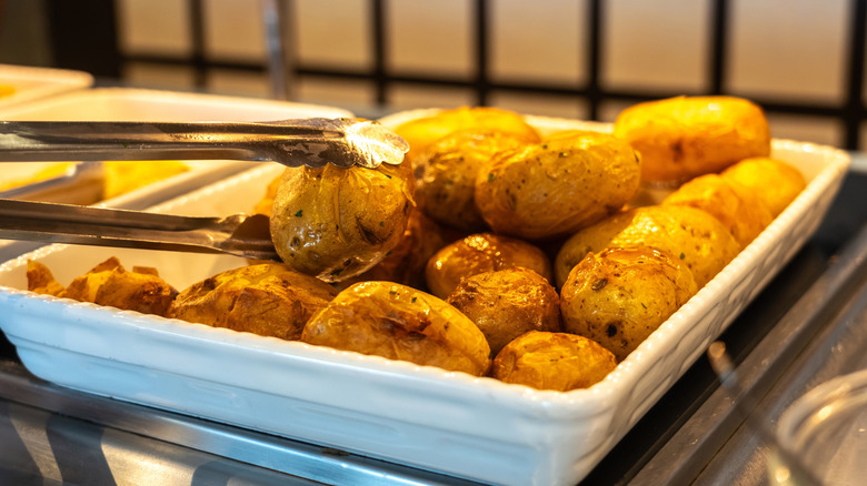 golden baked potatoes on a buffet with tongs