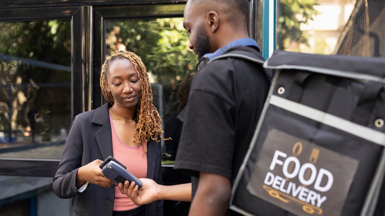 A person paying for a food delivery outside of a property, using their phone to do so