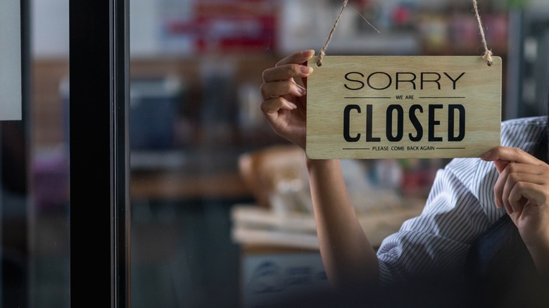 A "sorry we are closed" sign being turned around by a member of staff in the window