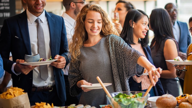 A group of people helping themselves to a buffet that includes a variety of food