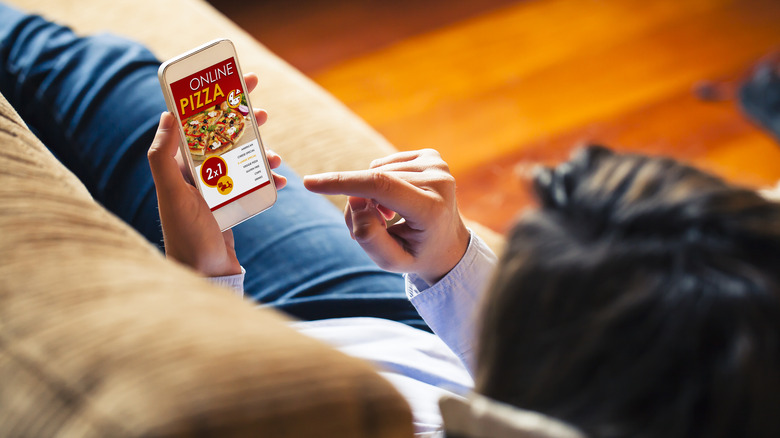 A person laying on a sofa looking at a phone that is showing them ordering pizza