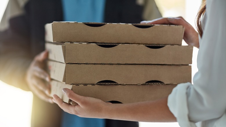A close up of four pizza boxes being delivered and passed to the recipient