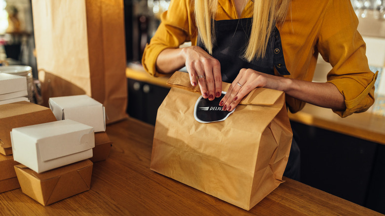A restaurant worker sealing a brown paper bag with a variety of other sealed packages shown