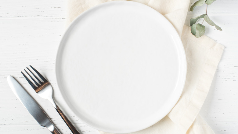 An overhead shot of a plain white plate with a napkin on one side and utensils on the other