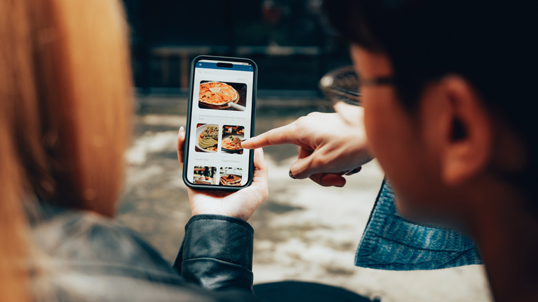 Two people looking at pictures of food on a smartphone, deciding what to order
