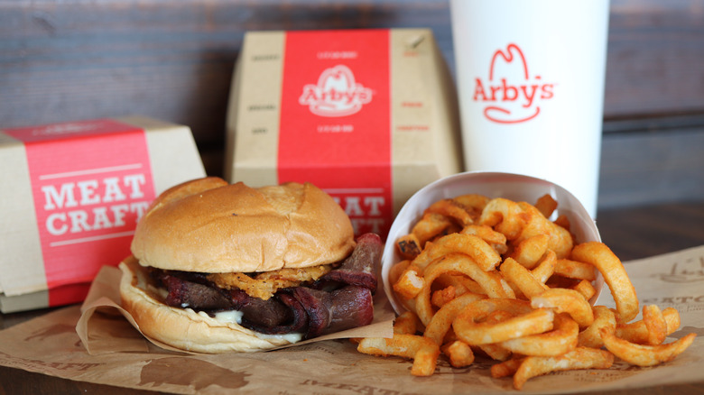 An Arby's sandwich, curly fries, and drink with Arby's boxes in the background