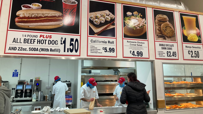 Costco food court counter with employees prepping orders and large menu images above
