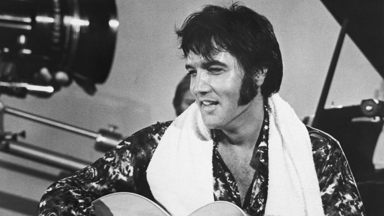 Elvis Presley smiling and playing guitar with a towel around his neck