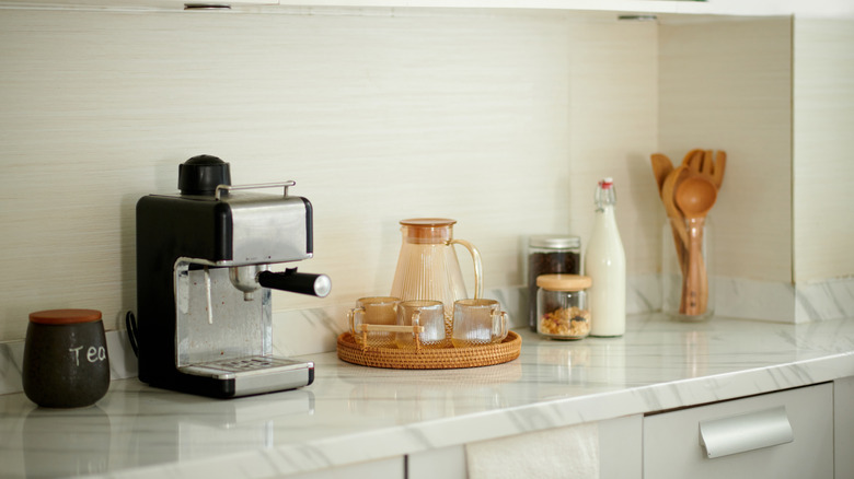 Coffee station with espresso machine, mugs, milk jar, utensils on counter