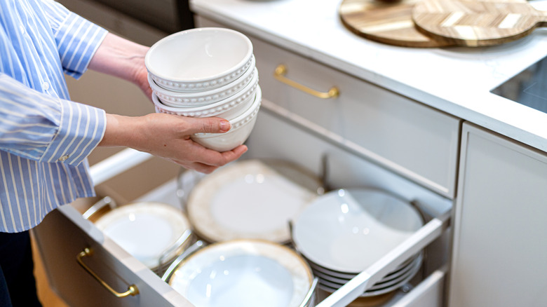 Hands putting bowls into drawer in kitchen