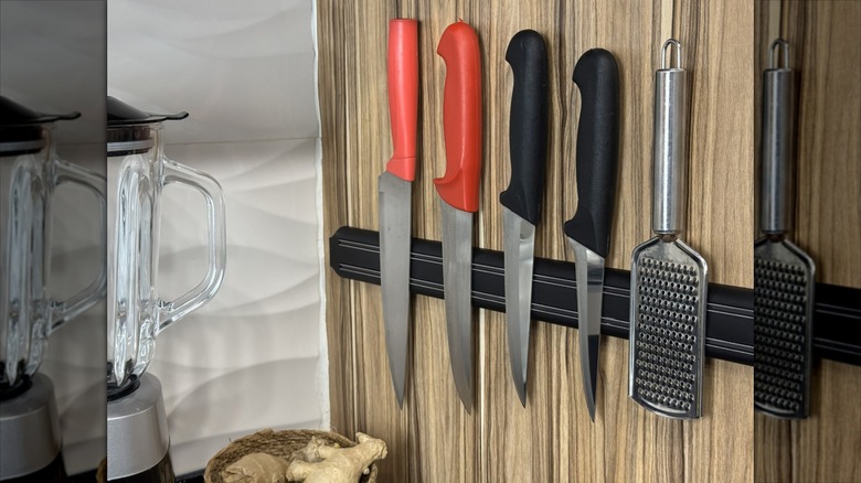 Knives and grater on metal magnetic wall strip in kitchen