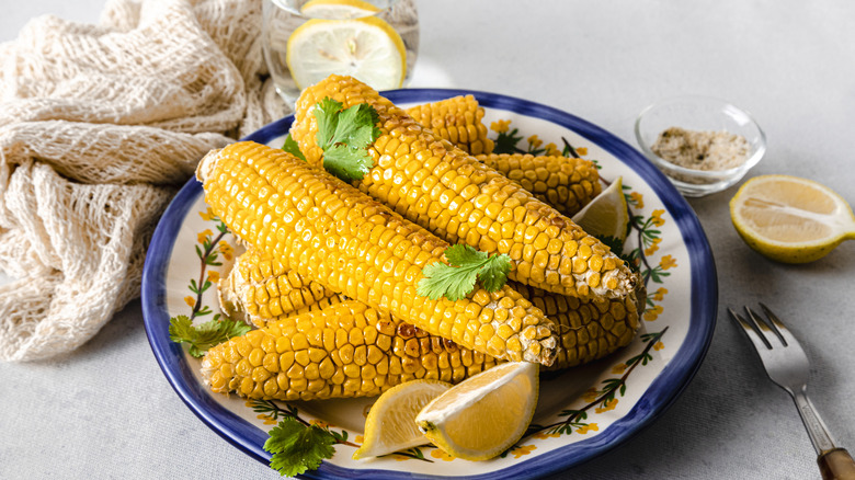 A bowl of stacked, bright corn on the cob with lemon and parsley
