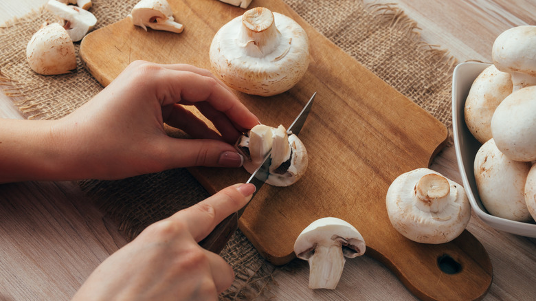 hands slicing mushrooms on a small wooden cutting board