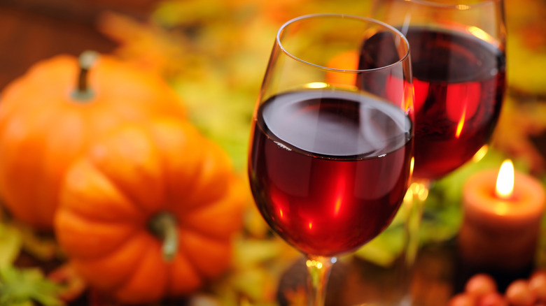 Two glasses of red wine sit in front of an autumnal landscape with pumpkins.
